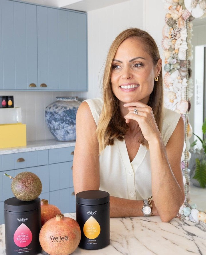 Woman smiling at a kitchen counter with fruit and products.